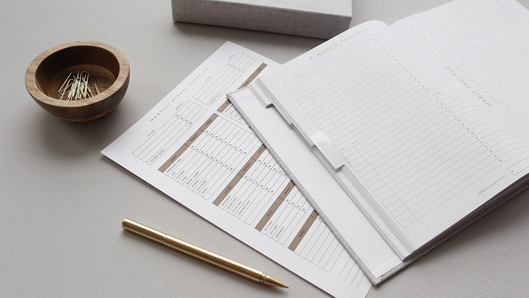 close up of financial paperwork on a white desk with a gold pen and a bowl of paper clips