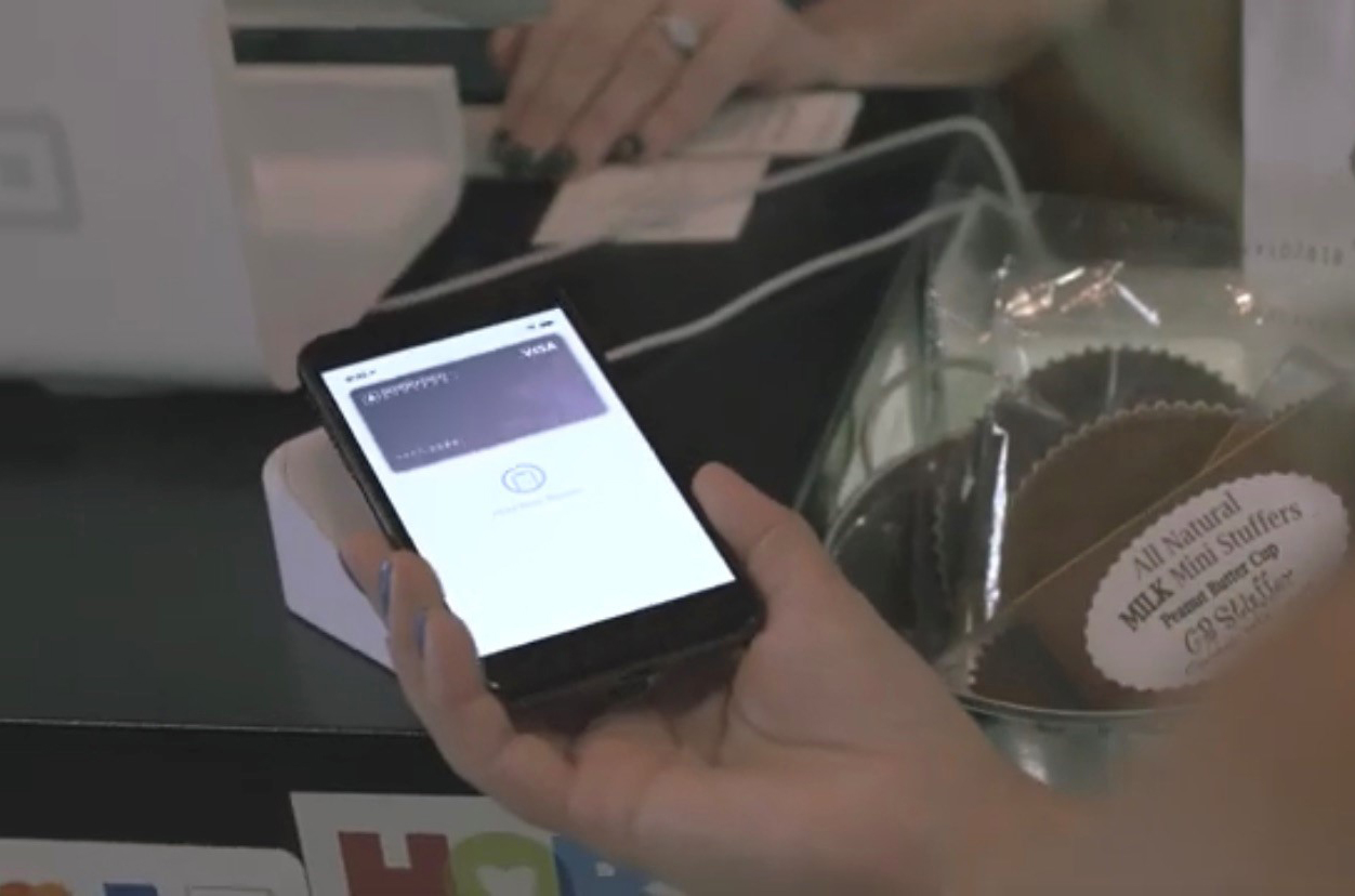 Person holding smartphone over contactless payment reader with image of Biddeford Savings debit card on the phone screen