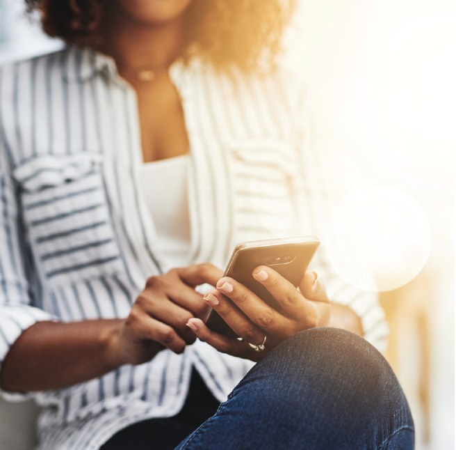 Woman in striped shirt using smartphone with diffused sunlight in the background